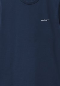 Granatowa koszulka z miękkiej bawełny, z okrągłym dekoltem i małym białym logo Carhartt na lewej stronie klatki piersiowej. Płaska tekstura.