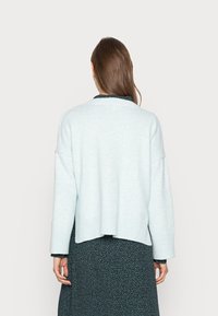 Pull bleu clair oversize avec un ourlet côtelé et des manches larges. Porté sur une robe florale foncée, avec un col rond.