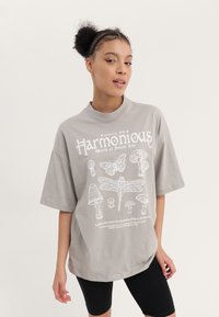 Gray oversized t-shirt with short sleeves featuring white graphic illustrations of flora and fauna, including mushrooms and a butterfly.