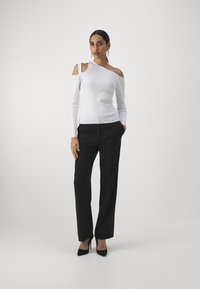 Top bianco a maniche lunghe con spalla scoperta, motivo testurizzato, abbinato a pantaloni neri a vita alta e décolleté neri a punta.