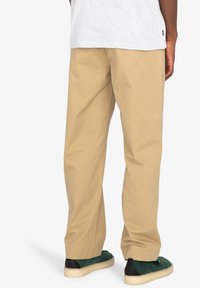 Khaki bavlnené nohavice so rovnými nohavicami, s hladkou textúrou a uvoľneným strihom. Nosené s tmavozelenými a čiernymi slip-on topánkami.