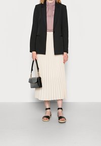 Černý tailored blazer, mauve plisovaná sukně, černá kabelka a černé sandály na kotníkových pasech. Minimalistický design, hladká textilie.