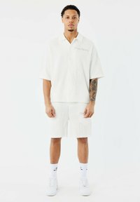 Conjunto de camisa de manga corta blanca y pantalones cortos con una tela texturizada que presenta contornos de cactus. Destacado por un logotipo bordado en la camisa.