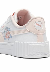 Biała skórzana tenisówka z różowymi akcentami, kwiatowym haftem po boku, grubą białą gumową podeszwą i wyraźnym logo „PUMA” na pięcie.