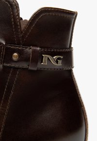 Bruine leren enkellaars met een gestikt ontwerp, een gladde textuur en een metalen logo-accent op de band.