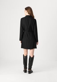 Rochie neagră, ajustată, cu mâneci lungi, talie evidențiată cu baretă și tiv evazat, asortată cu cizme negre din piele până la genunchi, dotate cu accente de lanț.