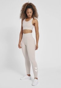 Lichtbeige sportset bestaande uit een crop top en high-waisted leggings. De leggings hebben witte chevronpatroonaccenten. Gecombineerd met witte sneakers.