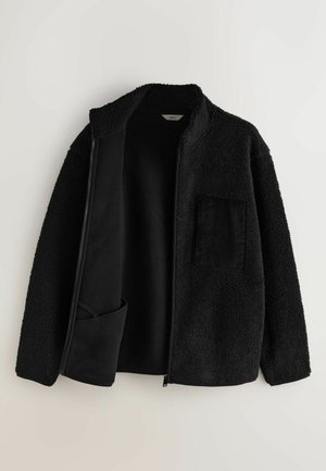 Svart zip-up jacka tillverkad av textilerad, fluffig tyg med en mjuk insida. Har en kordflodspocket på vänster sida.