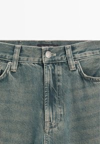 Jeans in denim blu sbiadito con chiusura a bottone, design a cinque tasche e cuciture visibili. L'etichetta riporta "Massimo Dutti."