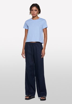 T-shirt cropped azzurro chiaro con maniche corte abbinato a pantaloni ampi blu scuro. Sandali con suola nera e dettagli hardware decorativi.