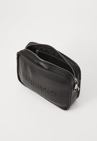 Custodia da viaggio in pelle nera con finitura testurizzata, dotata di una cerniera argentata e logo del marchio in rilievo sulla parte anteriore. Parzialmente aperta per rivelare la fodera.