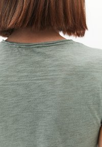 T-shirt a maniche corte di colore verde oliva con scollatura rotonda, realizzato in un tessuto morbido e leggero; texture leggera con variazioni sottili.