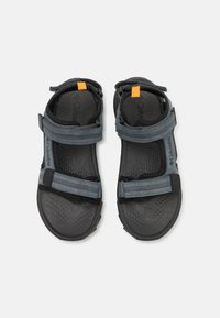 Sandales gris foncé avec des sangles réglables, semelle intérieure texturée et semelle extérieure en caoutchouc. Présente un accent orange sur la sangle supérieure. Design durable.
