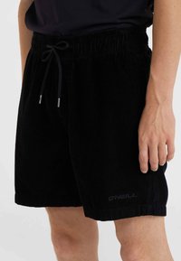 Black corduroy shorts with an elastic waistband, drawstring closure, and subtle branding on the hem. Soft texture and straight cut.
