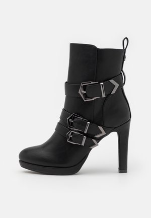 Czarny skórzany botek na wysokim obcasie, z trzema srebrnymi sprzączkami i paskami, szpiczasty nosek oraz pętelka z tyłu do zakładania.