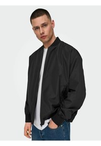 Black bomber jacket with a zip front, ribbed cuffs, and collar. Worn over a white T-shirt, paired with blue denim jeans. Smooth texture.