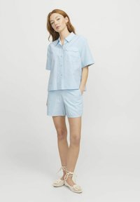 Camicia azzurro chiaro a maniche corte con bottoni e tasca, abbinata a pantaloni corti coordinati. Tessuto a righe, vestibilità casual e materiale leggero.