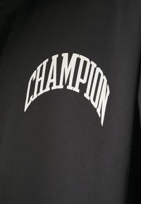 Czarny sweter z białym, łukowatym logo "CHAMPION" w pogrubionej czcionce. Wykonany z gładkiego materiału o delikatnej strukturze.