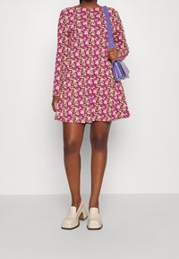 Mini abito floreale rosa, con maniche lunghe e gonna svasata. Abbinato a scarpe con tacco a blocco beige texturizzate e una piccola borsa viola.