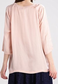 Vaaleanpunainen, löysä paita, jossa on kolme neljännestä pitkät hihat, sileä pinta, pyöreä kaula-aukko ja kaareva helma, yhdistetty tummansiniiseen pitsihameeseen.