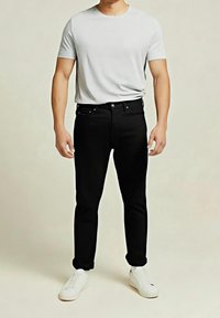 Jean noir coupe slim, design à cinq poches, bouton en métal et rivets, associé à un t-shirt gris clair à manches courtes et des baskets blanches.