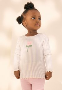 Langarmshirt in lichtblauwe en witte strepen, voorzien van een roze bloemendessin, gestructureerde stof en gegolfde randen. Gecombineerd met roze broek.