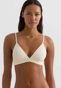 Krém színű háromszög alakú bralette texturált anyaggal, vékony állítható pántokkal és hullámos szegéllyel. Párnázás nélkül, könnyű kialakítás.