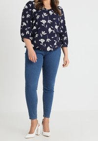 Laivansininen kukkakuosisia pusero, jossa on kolmanneksen mittaiset hihat, yhdistettynä sinisiin slim fit -farkkuihin ja valkoisiin korkokenkiin. Kukat ovat valkoisia.