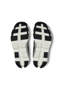 Scarpe da corsa in bianco e nero viste dal fondo, che mettono in evidenza le suole in gomma testurizzate con motivi di battistrada geometrici.