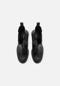 Sapatos de couro preto com um design elegante, apresentando um cabedal liso, detalhes perfurados e painéis laterais elásticos para facilitar o calçar.