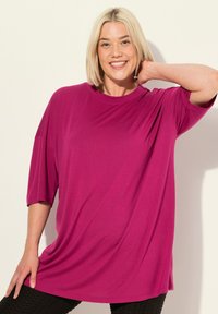 Losse, kortekorte, magenta top van zachte stof, met een ronde hals en een relaxte silhouette. G gedragen met gestructureerde donkere legging.