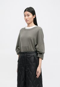 Pilkas megztinis su plačiu apykakle, derinamas su juodomis ketinčiomis plačiomis kelnėmis, turinčiomis raištelį juosmens srityje ir šoninėmis kišenėmis.