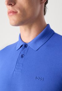 Polo azul feito de tecido texturizado com colarinho abotoado. Apresenta um logotipo 'BOSS' na mesma cor no peito.
