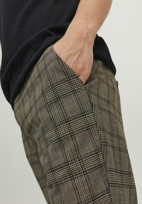 Brune ternede bukser med et struktureret stof, sidelommer og en skræddersyet pasform, med et subtilt mønster af vekslende tykke og tynde linjer.