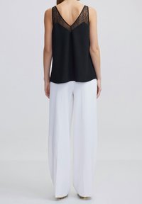 Black sleeveless top with a lace back detail, V-neck design, paired with white wide-leg trousers and sleek golden accents at the hem.