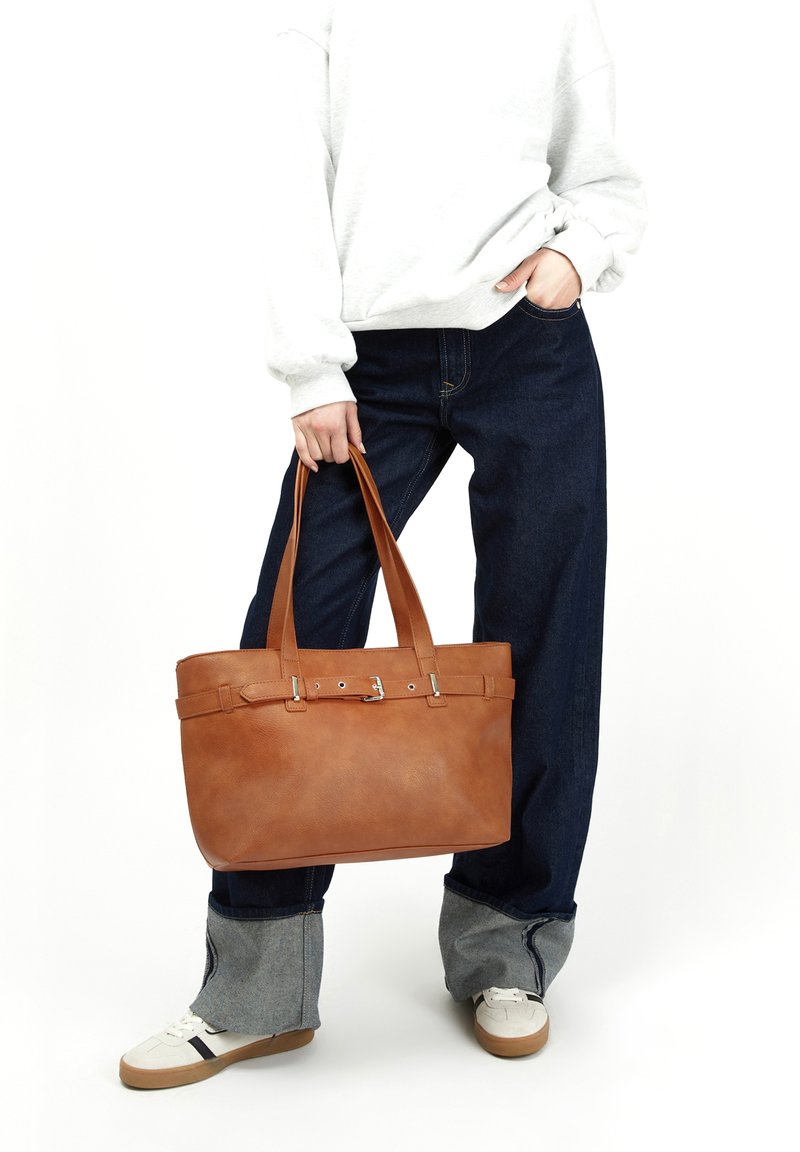 Brun läder tote-väska med platt botten, två robusta handtag och silverdetaljer. Slät yta med en strukturerad form.