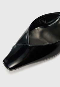 Černá laková kožená bota s špičatou špičkou a výřezem ve tvaru V. Hladký povrch a minimální detaily hardware. Velikost EUR 37.