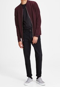 Burgundy bomber jacket with a zip front, black t-shirt, black tapered pants, and light gray sneakers with white soles. Plain textures throughout.