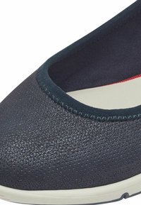 Chaussure bleu foncé avec une surface texturée, bout rond, bord élastique et semelle blanche. L'intérieur présente des accents rouges.