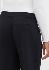 Black trousers with a smooth fabric, featuring a back pocket and straight-leg design, paired with a white long-sleeve top.