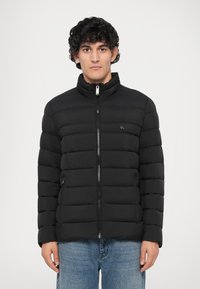 Jachetă puffer neagră cu guler înalt, design matlasat orizontal, fermoar frontal și buzunare laterale. Materialul pare neted și ușor.