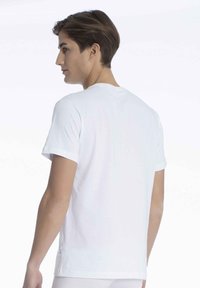 Hvid bomulds t-shirt med kort ærme, der har en rund halsudskæring, rene linjer og en lille mærkat på den nederste venstre side nær sømmen.