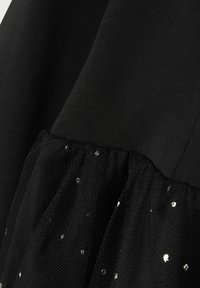 Svart klänning med en texturerad överdel och en lager av tyllkjol, prydd med silverpaljetter för extra detaljer och visuell intresse.