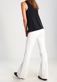 Jeans bianchi a zampa d'elefante con una texture liscia, abbinati a un top nero senza maniche, visti da dietro. Silhouette casual e aderente.