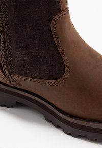 Stivale alla caviglia in pelle marrone con zip laterale, dettagli in camoscio, superficie texture e suola in gomma robusta con design antiscivolo.
