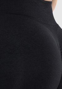 Svarta högmidjade leggings med en slät, elastisk textur. Tyget är matt och följsamt, vilket framhäver kroppens kurvor.