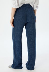 Marineblauwe, gestructureerde broek met een wijde pijp en elastische tailleband, met verticale strepen en een ontspannen pasvorm, weergegeven vanaf de achterkant.