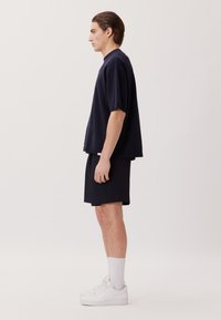 Top corto a maniche corte blu navy con scollo rotondo, abbinato a pantaloni corti neri e sneakers bianche. Design semplice con una vestibilità rilassata.