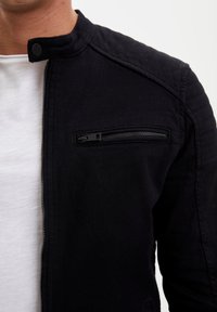 Czarna kurtka ze stójką, wyposażona w zapinaną na zamek kieszeń na piersi, teksturowane akcenty na ramionach oraz gładkie wykończenie materiału.