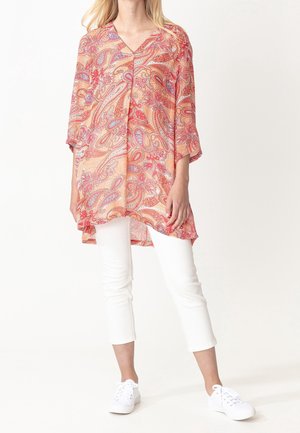 Tunique longue et ample de couleur orange vif avec un motif cachemire, dotée d'un col en V et de manches trois-quarts, assortie à un pantalon blanc et des baskets.